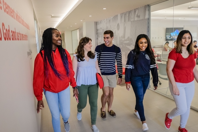 Group of students walking down the hallway discussing their M.B.A. studies.