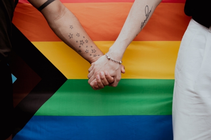 holding hands in front of LGBTQ+ flag