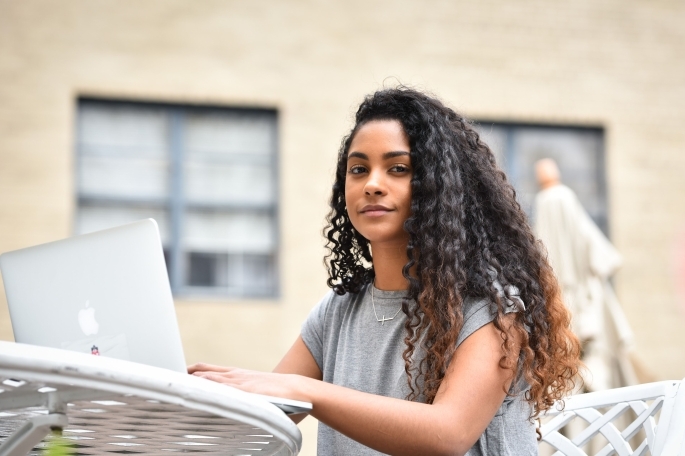 St. John’s University female student typing on laptop while sitting at a table outside.
