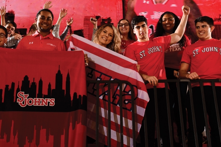 Fans cheering at basketball game holding St. John's flags
