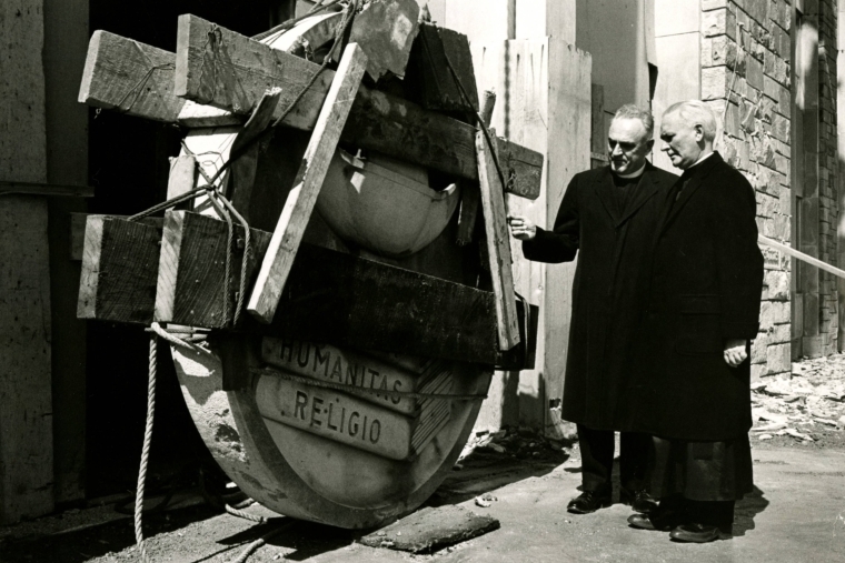 Very Rev. Edward J. Burke, C.M., President of St. John's University (right) examining the 16 foot diameter seal before it is hoisted into place above the entrance of St. Augustine Hall in 1964.