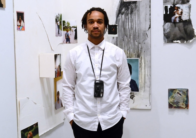 Kalen Roach standing in front of white wall of photographs