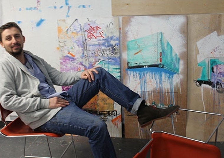 Henry Cunningham ’15C sitting in front of his canvasses