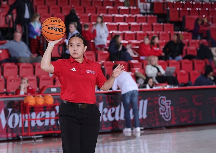 Women holding a basketball in a red shirt behind stadium seating 