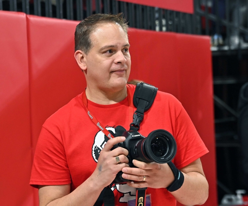 Wendell Cruz, Esq. ’91SVC, holding a camera on the sidelines of Carnesecca Arena 