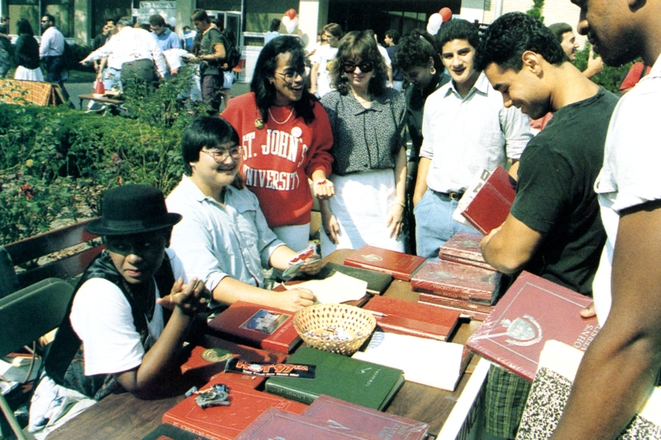 A student shows their school spirit with a red  St. John's sweatshirt and a few student organization pins at the activity fair, c. 1990.