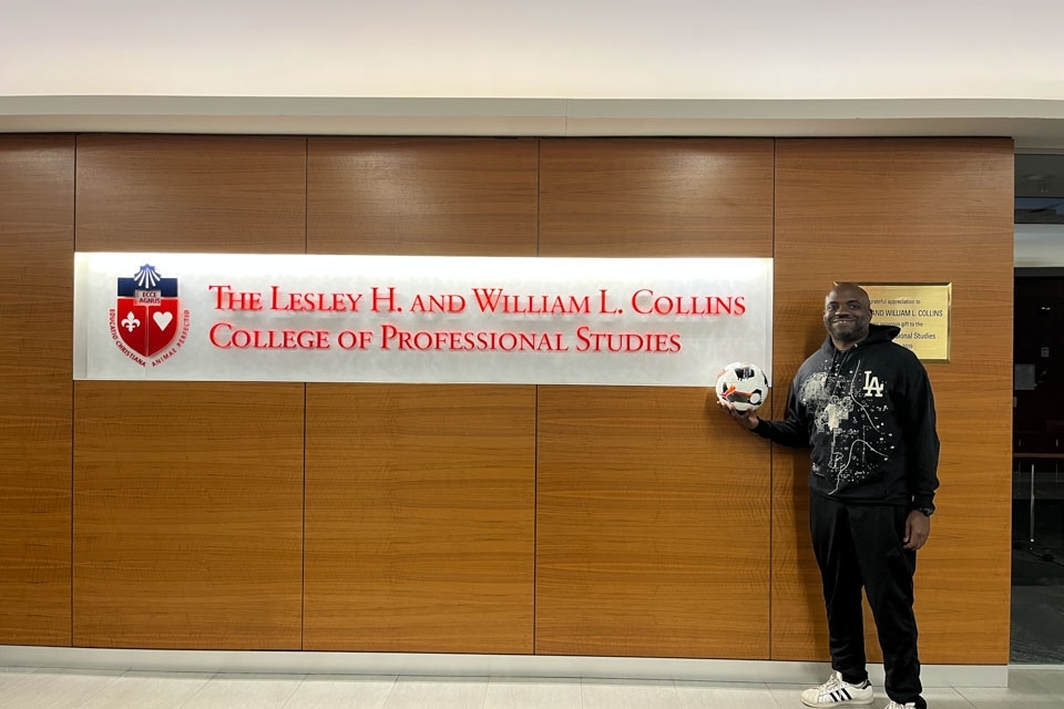Man standing next to sign that says "The Lesley H. and William L. Collins College Of Professional Studies" 