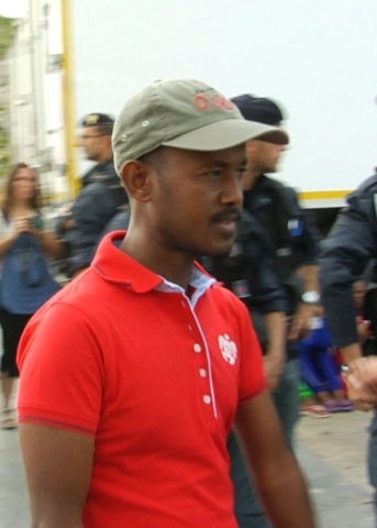 Man in a red shirt walking in the street surrounding by law enforcement