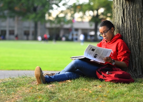 St. John's student reading while sitting against a tree