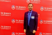 Dr. Bukhari in front of red background with multiple St. John's University logos