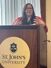 Maria Mello speaking at podium with St. John's University logo on it