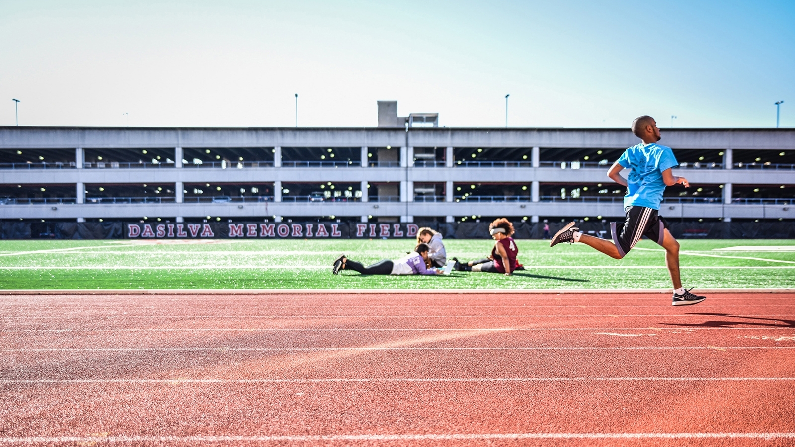 Male student running track while 2 other students study
