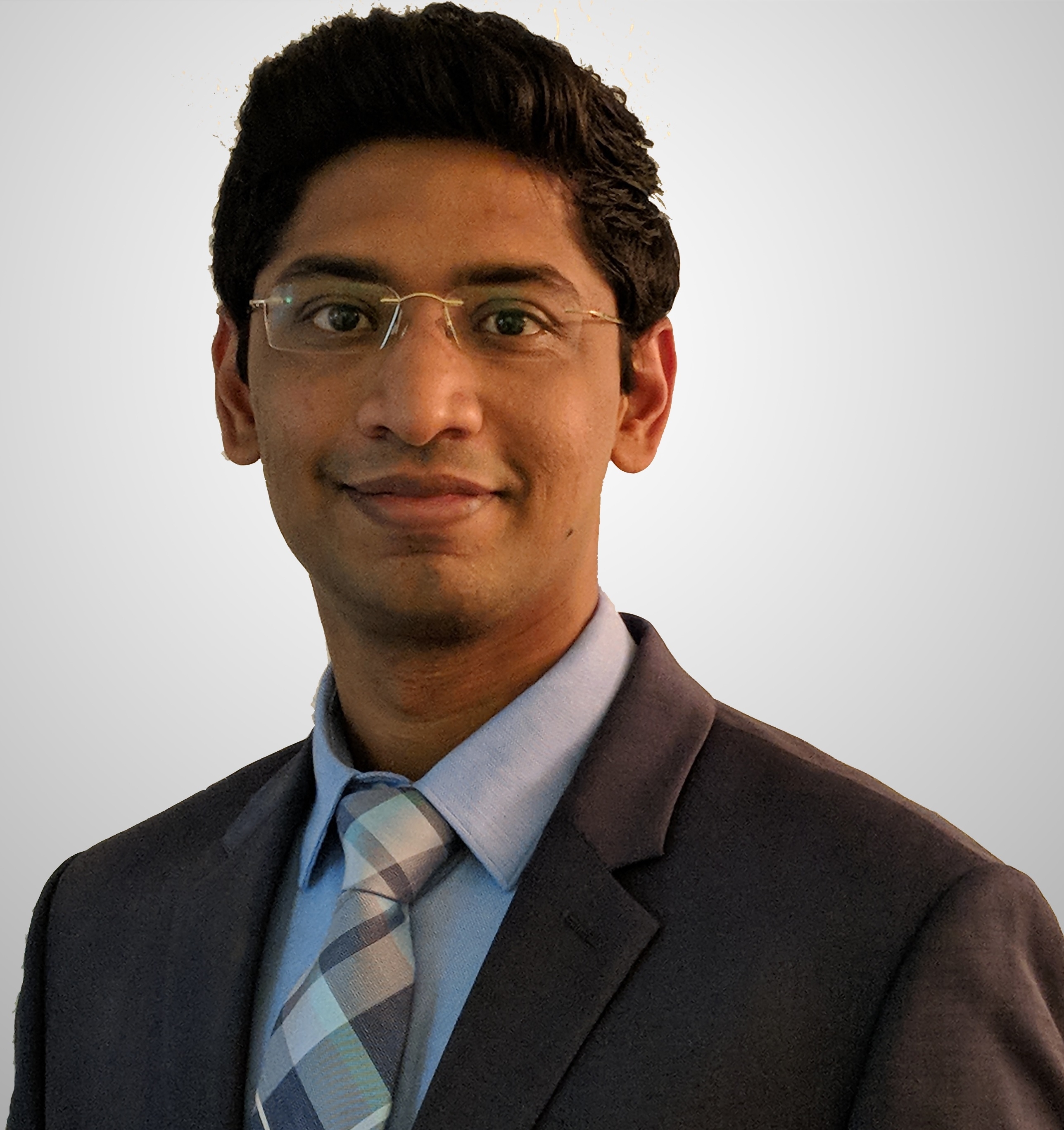 Professional headshot of professor, Dr. Nitesh Kunda in a gray blazer, blue button shirt, plaid tie and white background