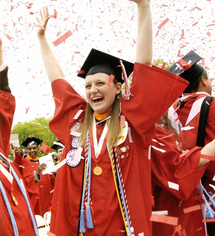 A student cheering at commencement wearing graduation cap and gown.