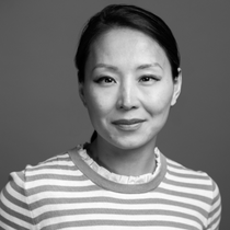 A black and white headshot of Cindy Chen Delano wearing a striped shirt.