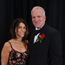 Denise and Michael Mattone stand for a photo in front of a black background.