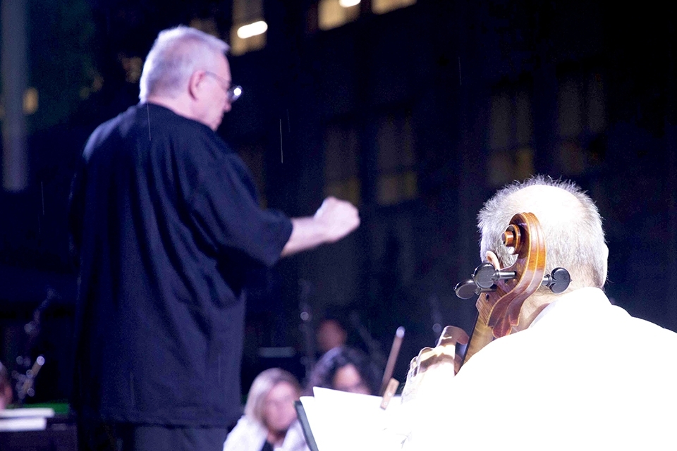 Inset of conductor and back view of man playing cello