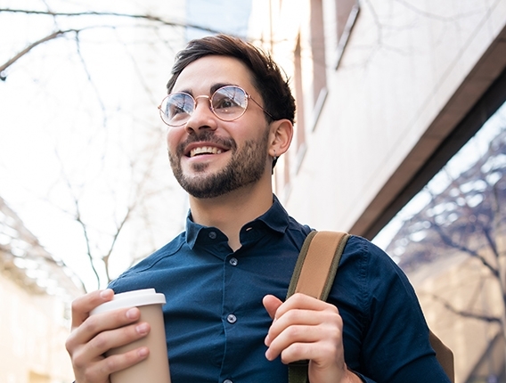 Man carrying a coffee outside and smiling